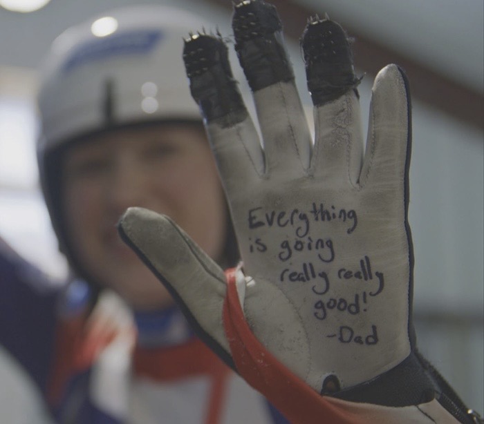 Luge athlete holding up a glove with a handwritten message from her father