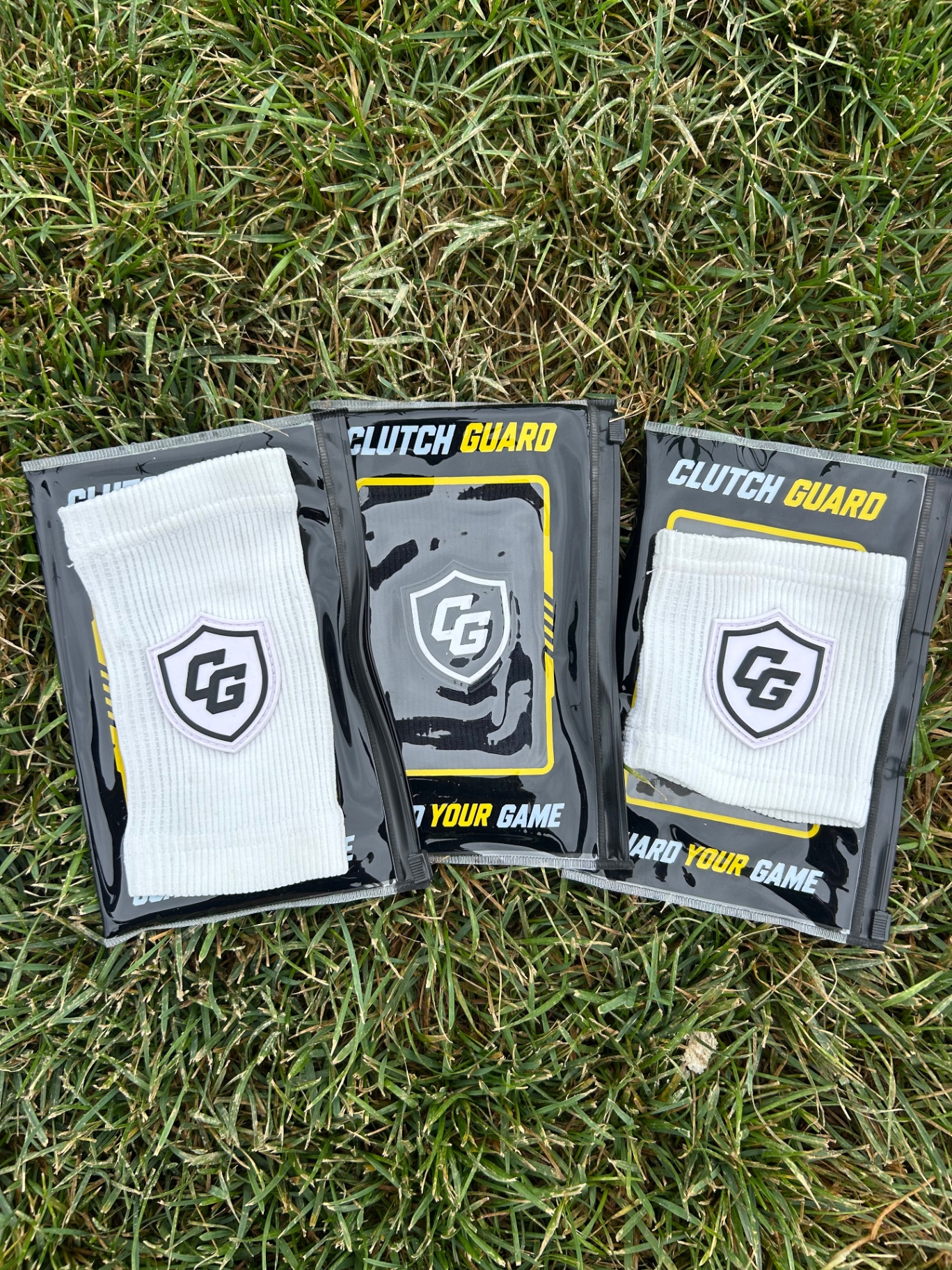 Three packaged white Clutch Guard wristbands on grass